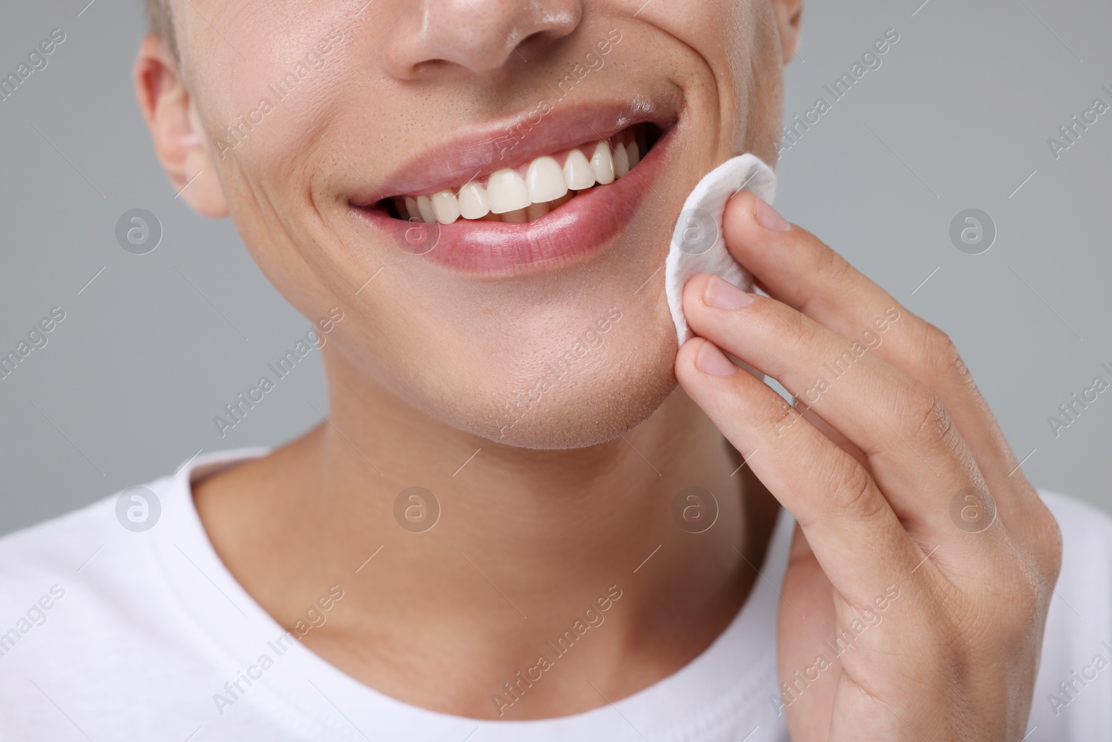 Photo of Man cleaning face with cotton pad on grey background, closeup