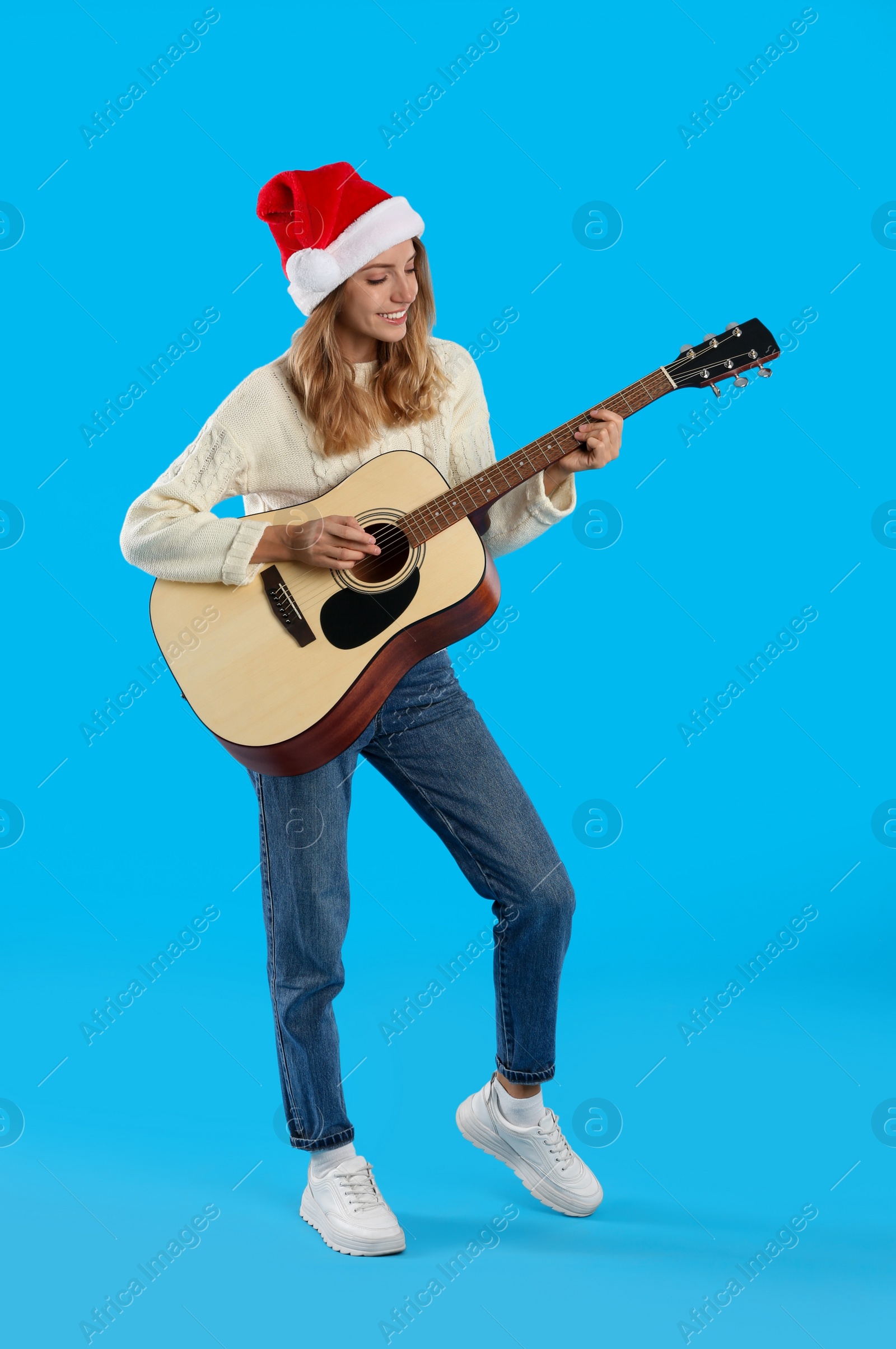 Photo of Young woman in Santa hat playing acoustic guitar on light blue background. Christmas music