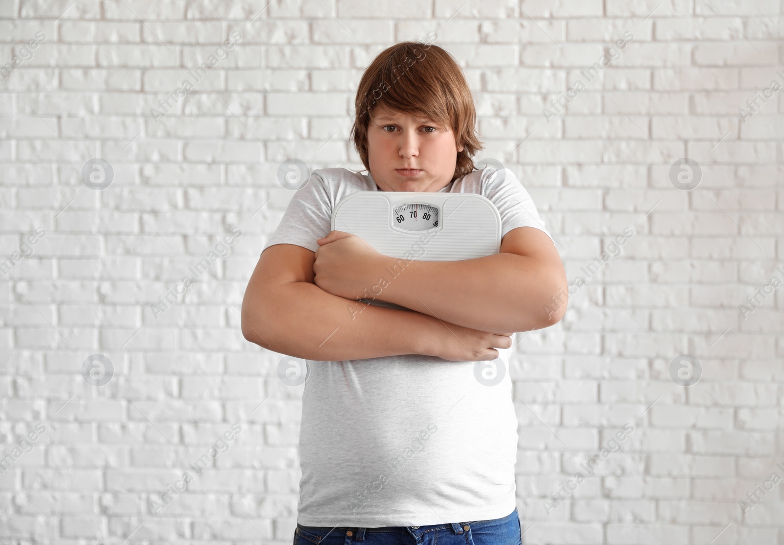 Photo of Emotional overweight boy with floor scales near white brick wall