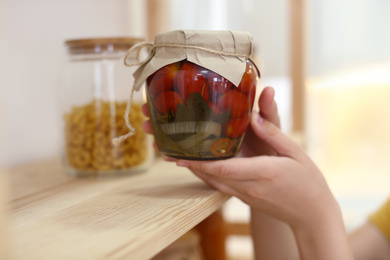 Photo of Woman putting jar of pickled vegetables on shelf indoors, closeup