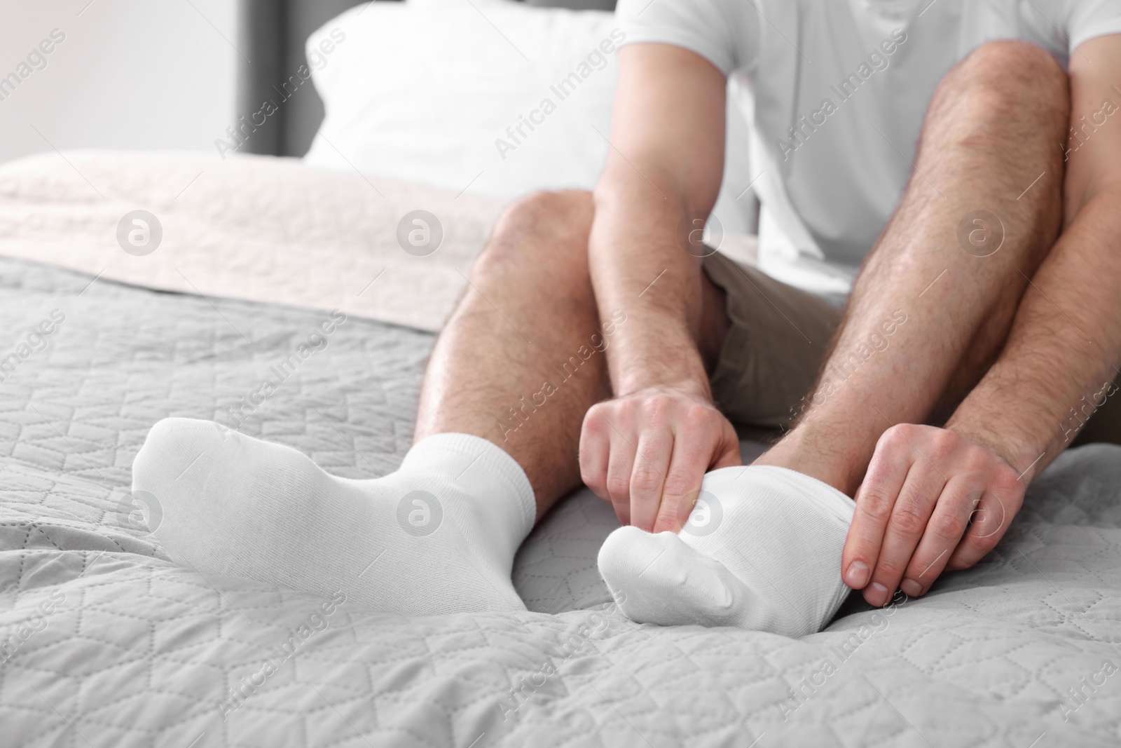 Photo of Man putting on white socks at home, closeup