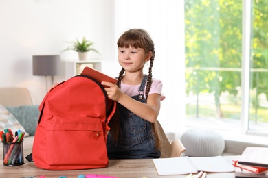 Photo of Schoolgirl putting stationery into backpack at home