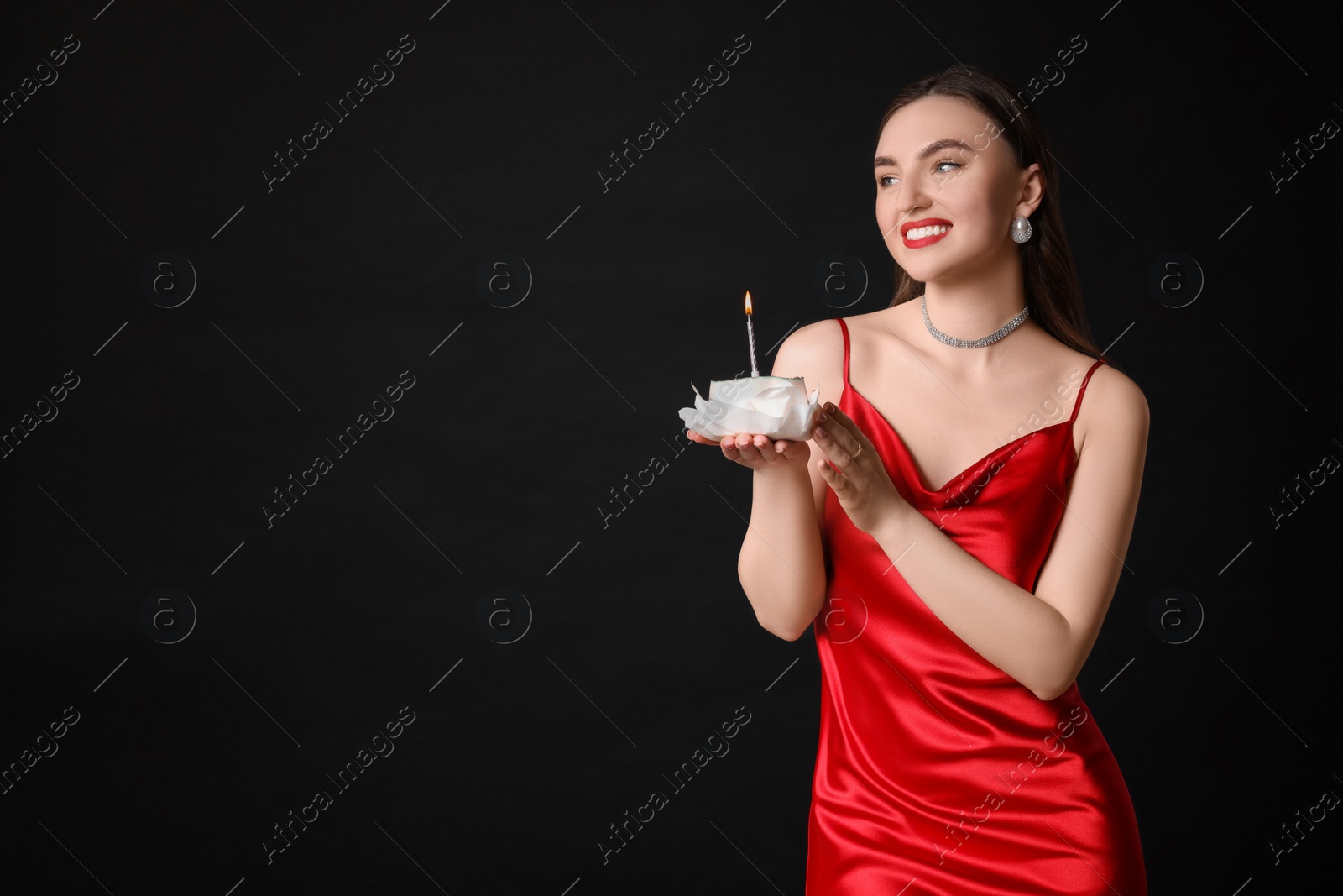 Photo of Attractive young woman holding her Birthday cake with burning candle on black background, space for text