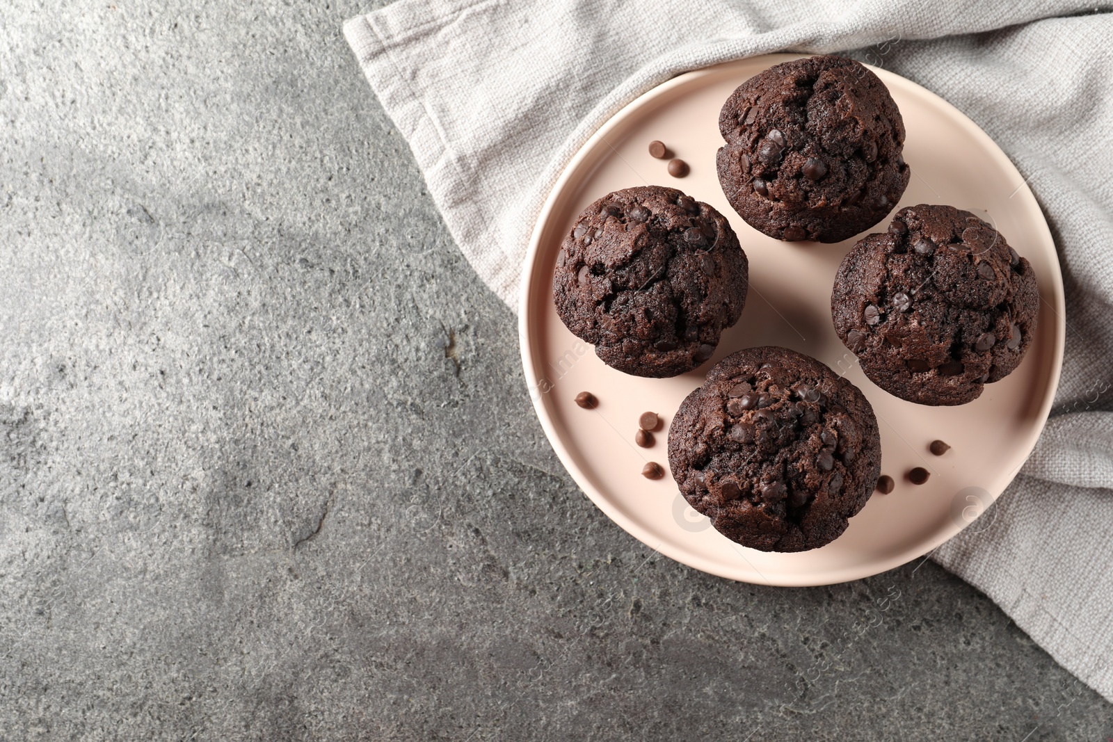 Photo of Delicious chocolate muffins on grey textured table, top view. Space for text