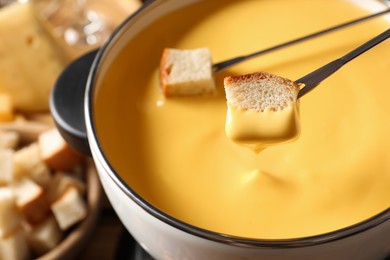 Photo of Dipping pieces of bread into tasty cheese fondue, closeup