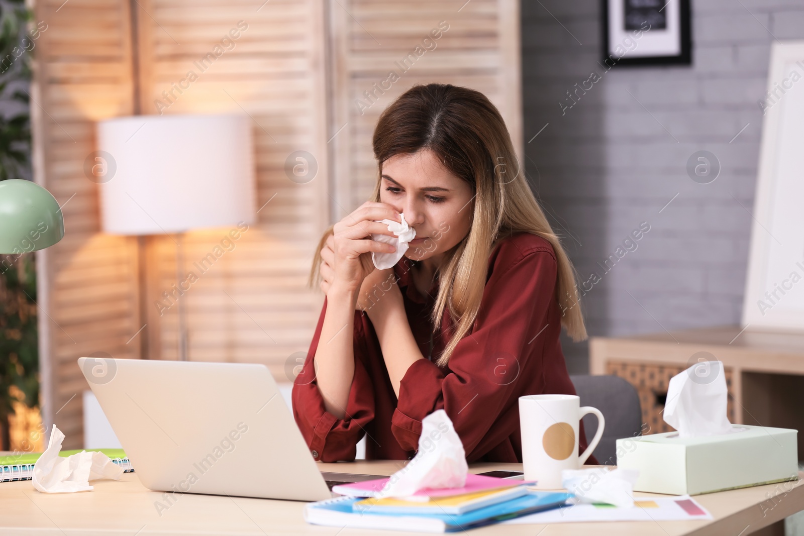 Photo of Sad woman with tissue suffering from cold while working with laptop at table