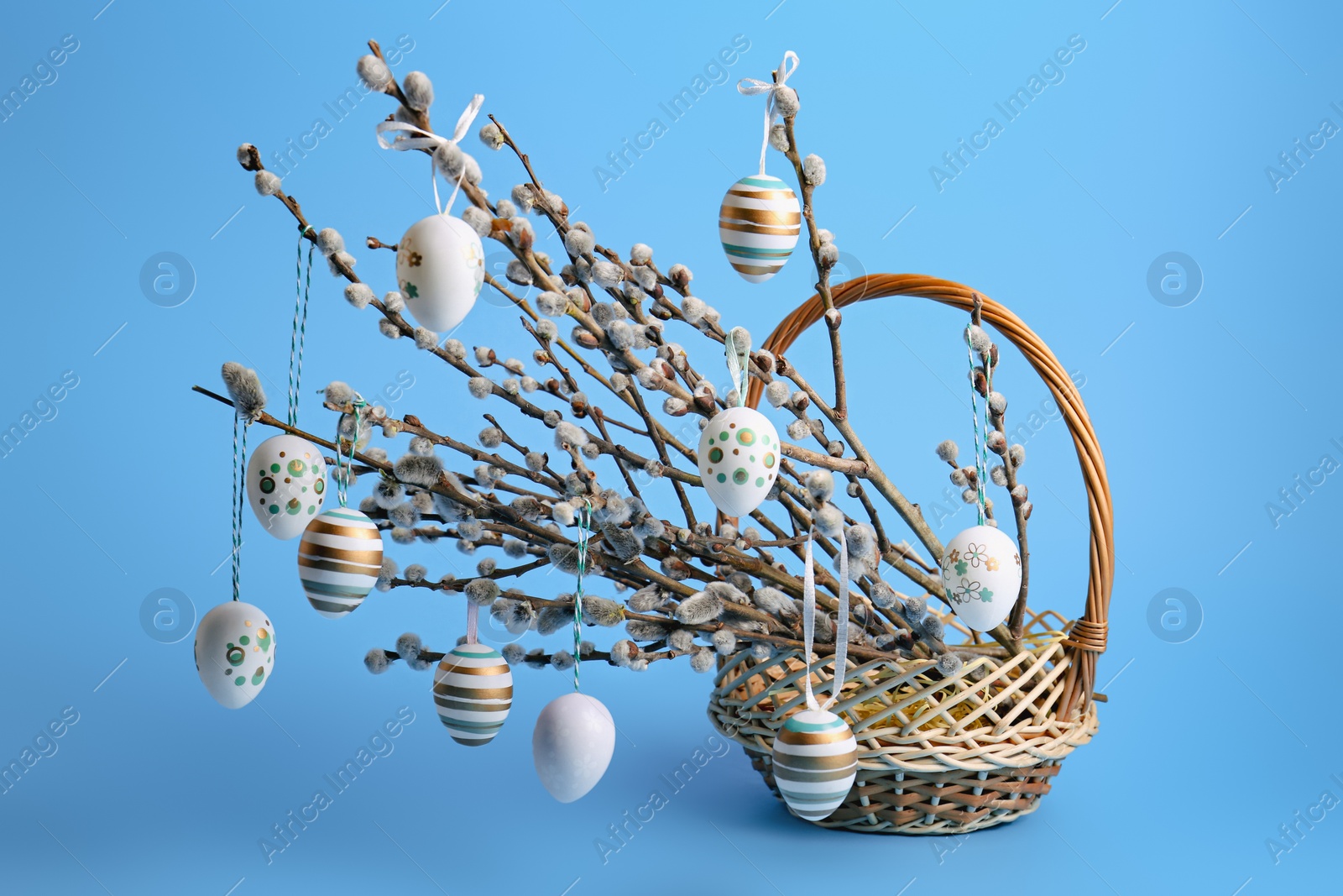 Photo of Wicker basket with beautiful willow branches and painted eggs on light blue background. Easter decor