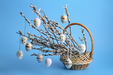 Wicker basket with beautiful willow branches and painted eggs on light blue background. Easter decor