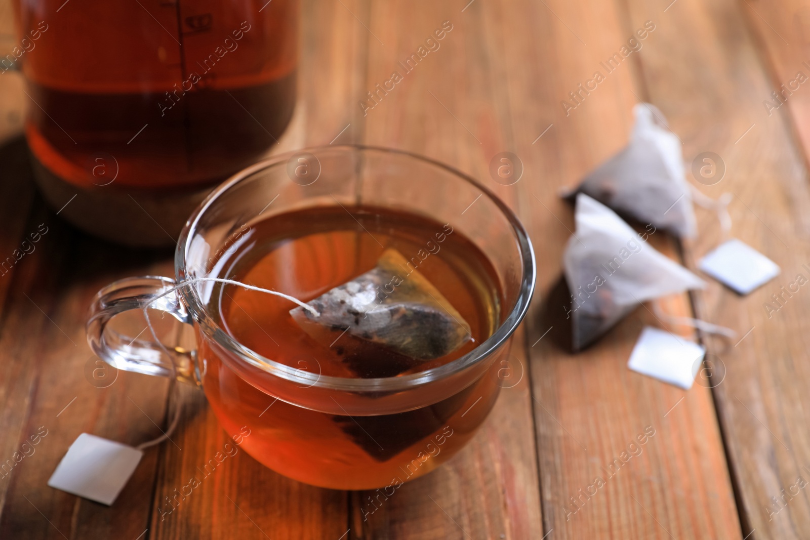 Photo of Tea bag in glass cup on wooden table, closeup