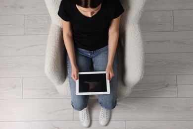 Photo of Woman working with tablet in armchair, top view