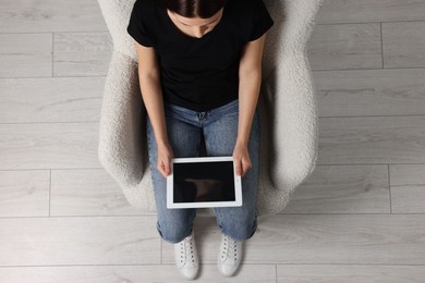 Woman working with tablet in armchair, top view