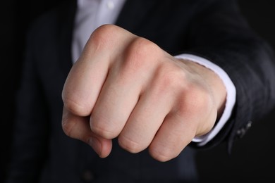 Photo of Businessman showing fist with space for tattoo on black background, closeup