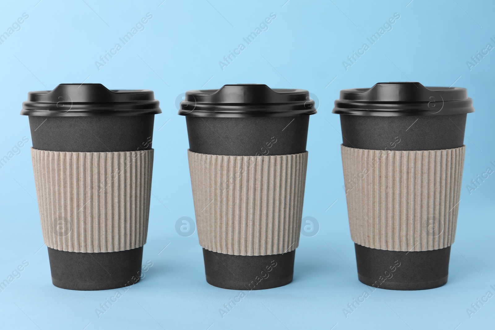 Photo of Paper cups with black lids on light blue background. Coffee to go