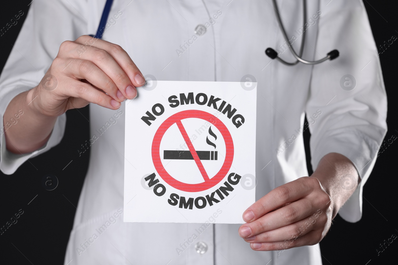 Photo of Doctor holding card with no smoking sign on black background, closeup