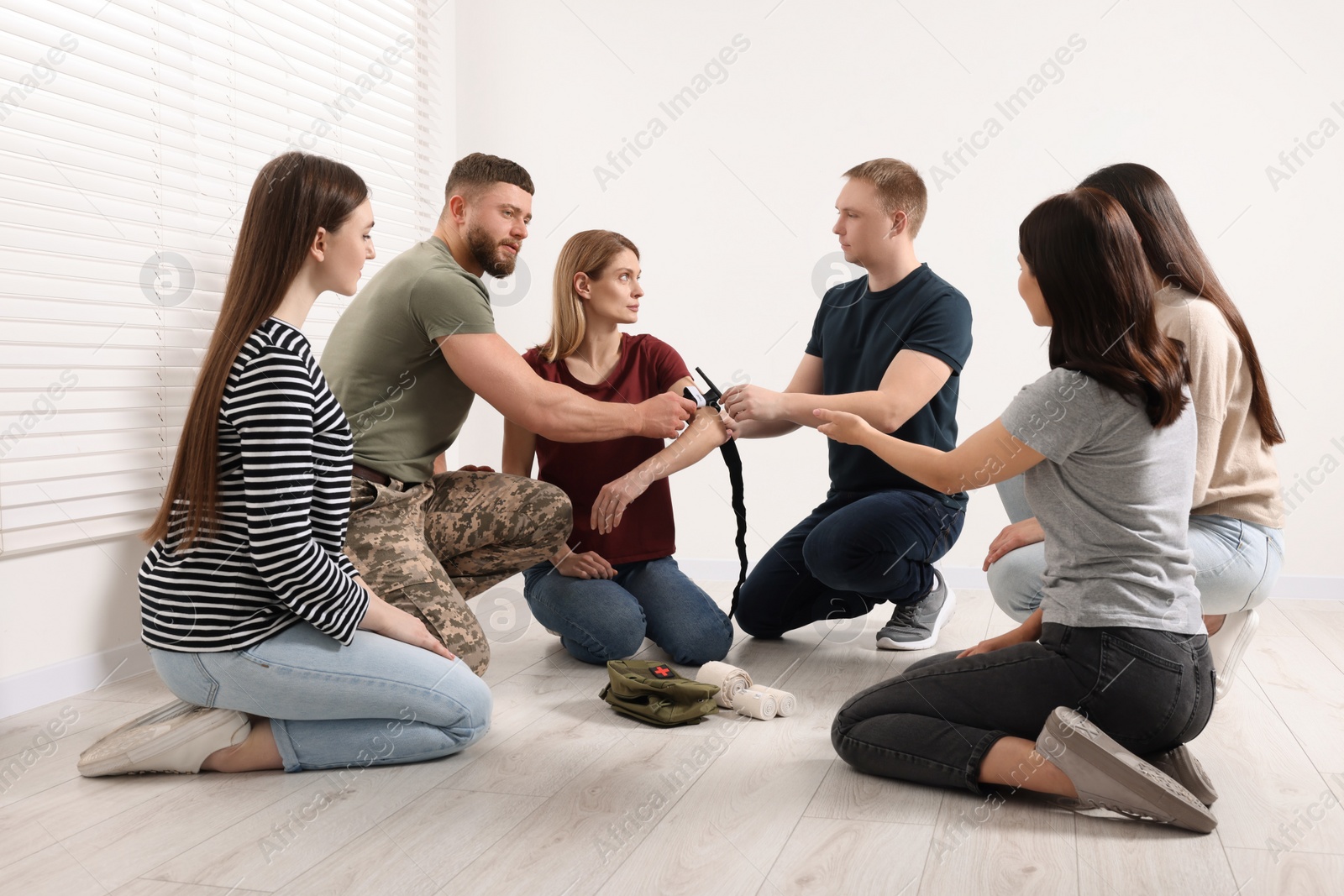 Photo of Soldier in military uniform teaching group of people how to apply medical tourniquet indoors