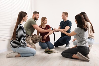 Photo of Soldier in military uniform teaching group of people how to apply medical tourniquet indoors