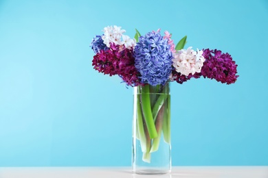 Photo of Beautiful hyacinths in glass vase on table against color background, space for text. Spring flowers