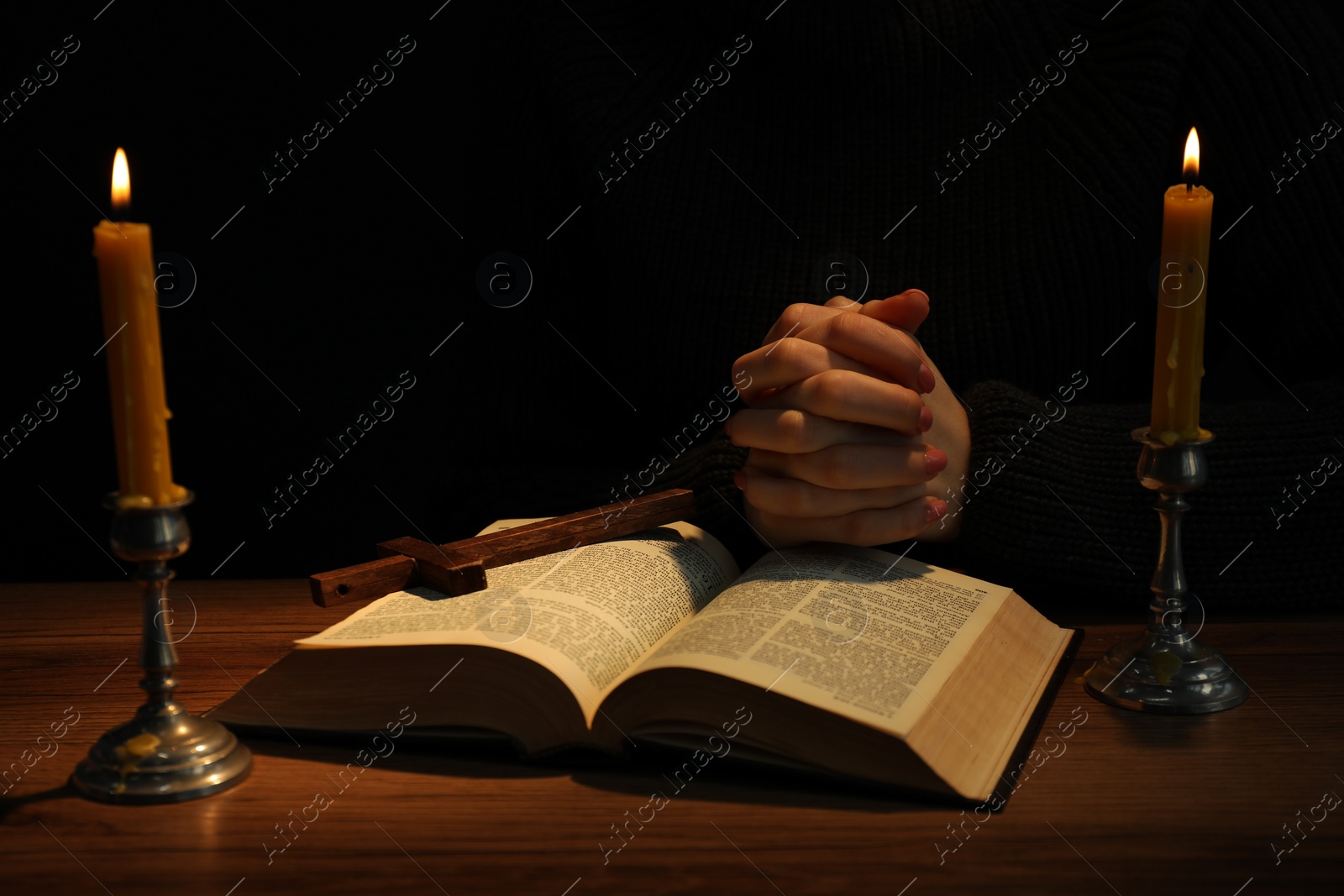 Photo of Woman praying at table with burning candles and Bible, closeup