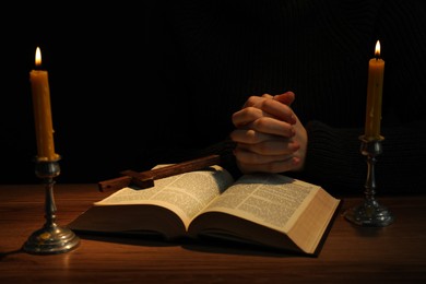 Woman praying at table with burning candles and Bible, closeup