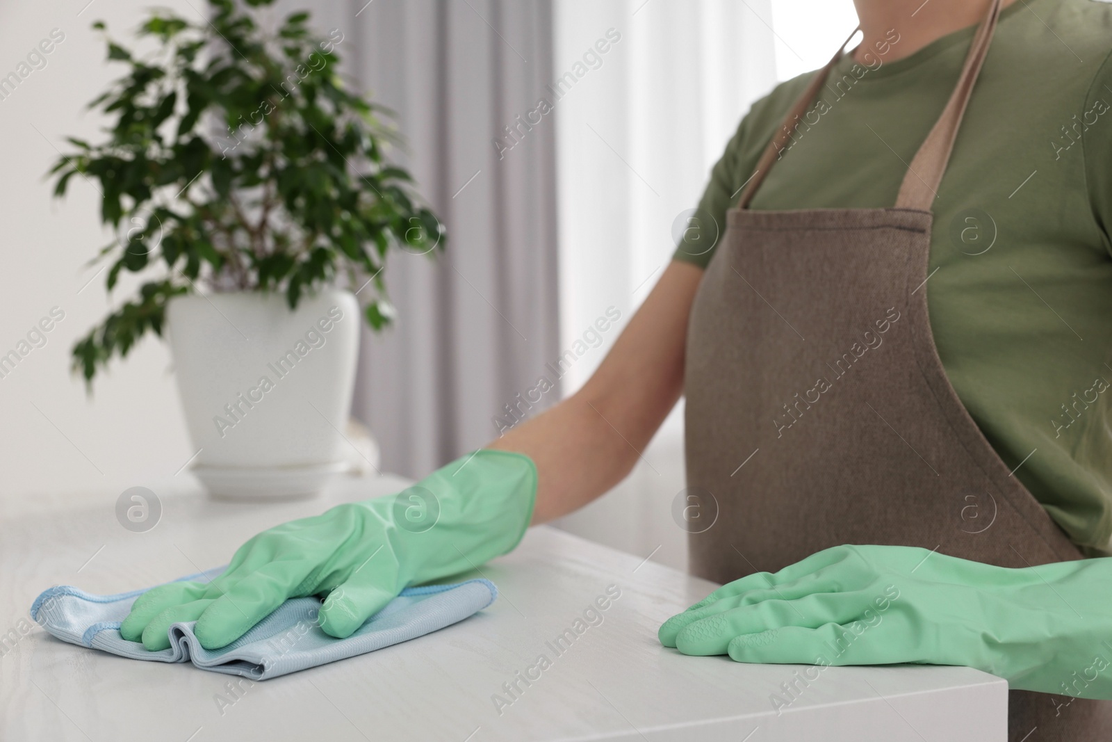 Photo of Woman with microfiber cloth cleaning white table in room, closeup