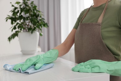 Woman with microfiber cloth cleaning white table in room, closeup