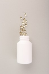 Photo of Bottle and vitamin capsules on light grey background, top view