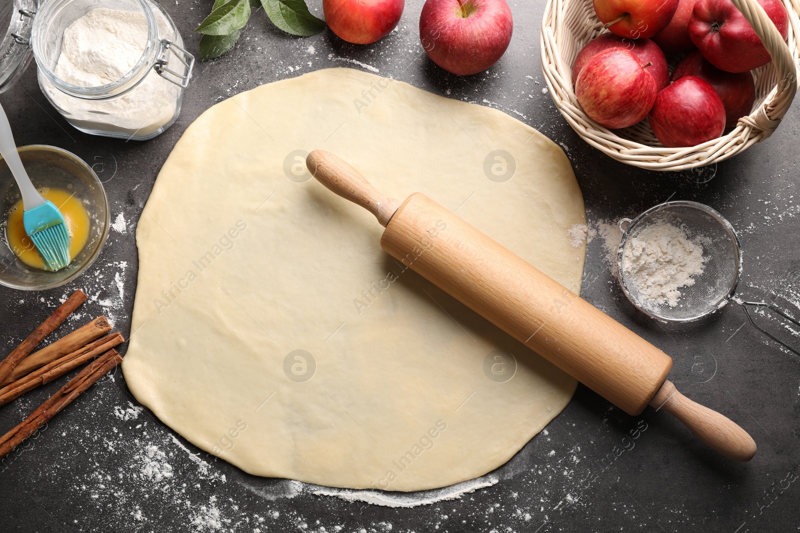 Photo of Fresh dough, rolling pin and ingredients on grey table, flat lay. Making apple pie