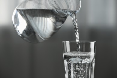 Pouring water from jug into glass on blurred background, closeup