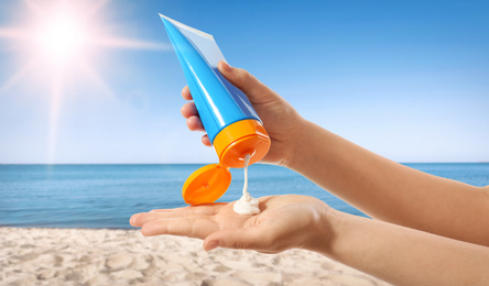 Young woman applying sun protection cream near sea, closeup