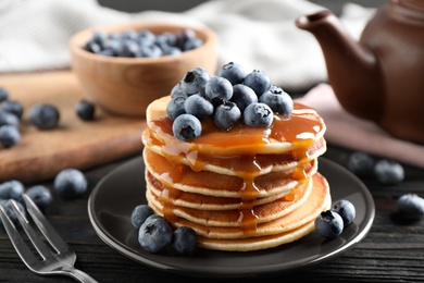 Photo of Delicious pancakes with fresh blueberries and caramel syrup on black wooden table