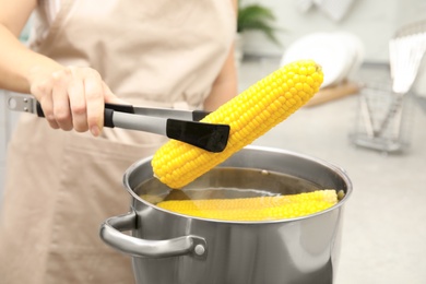 Woman taking boiled corn from pot with tongs in kitchen, closeup