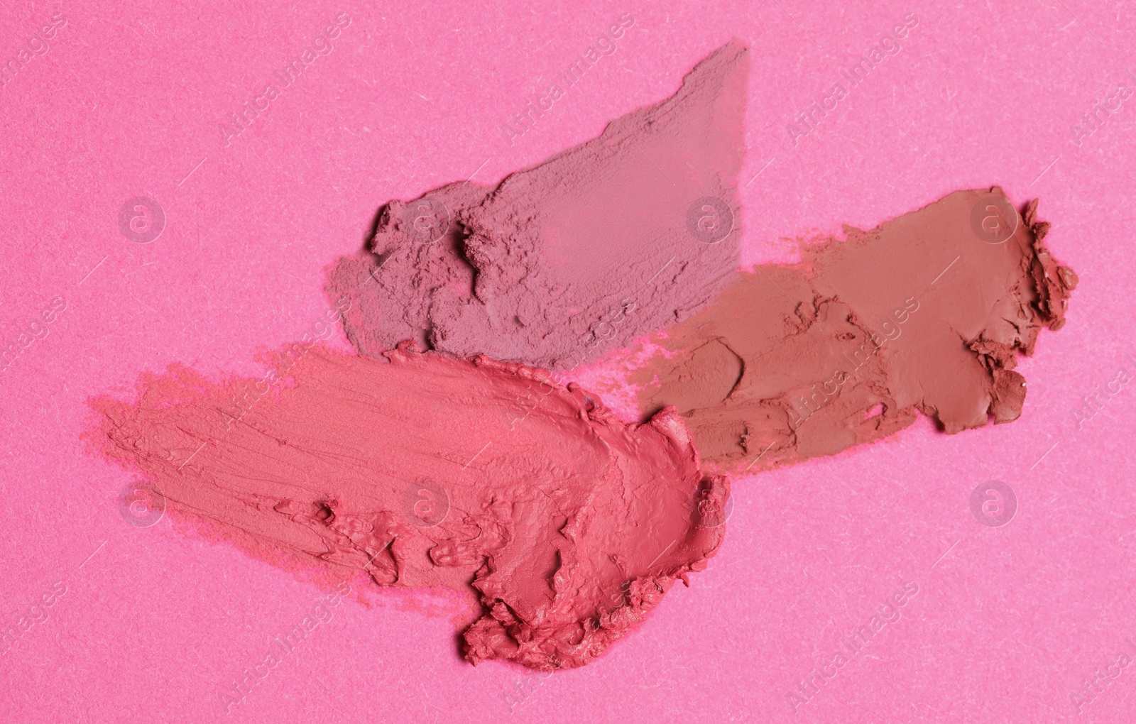 Photo of Smears of beautiful lipsticks on pink background, top view