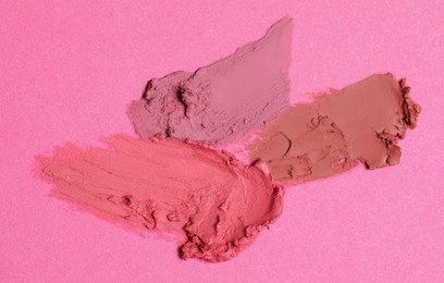 Photo of Smears of beautiful lipsticks on pink background, top view