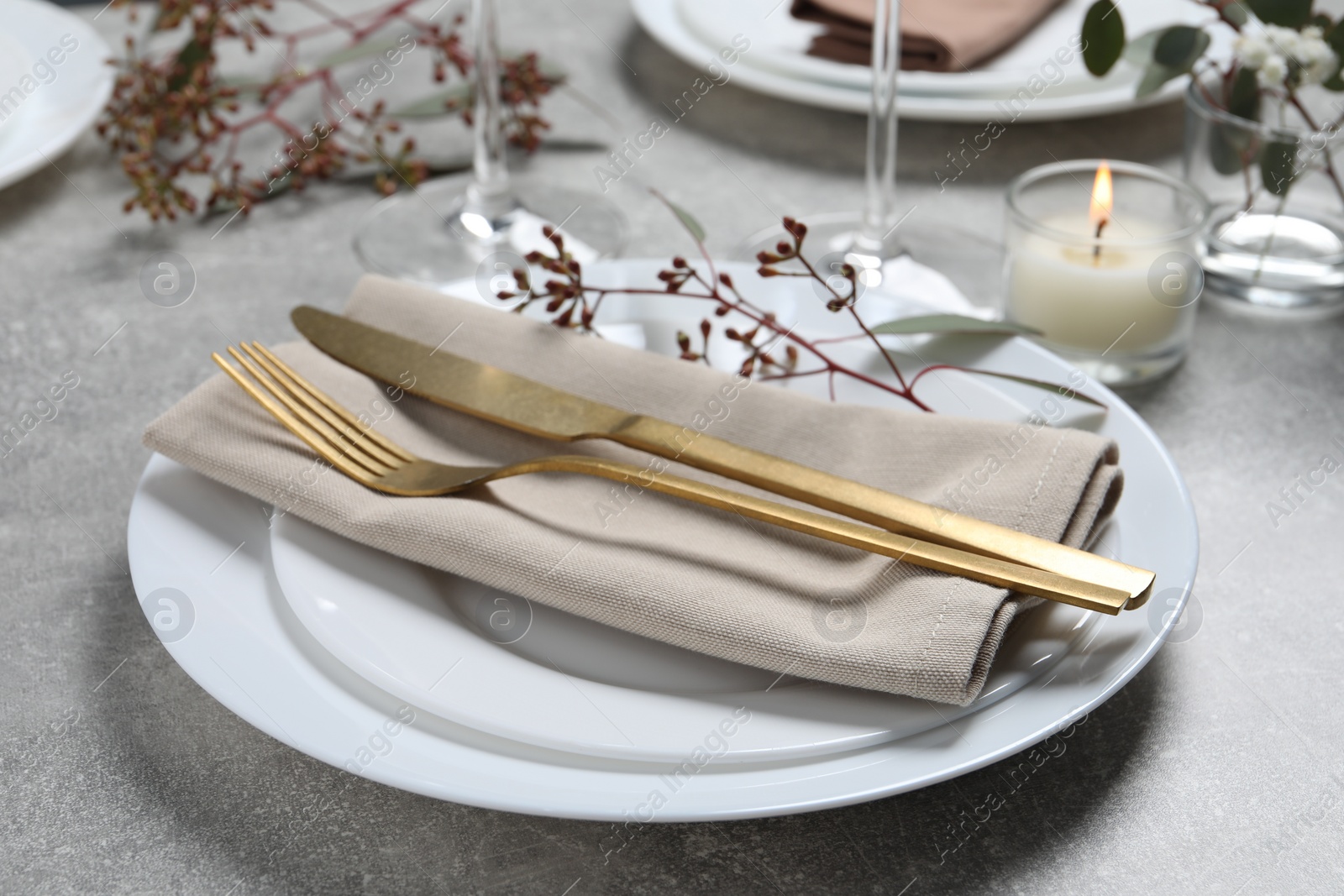 Photo of Stylish table setting with cutlery, burning candle and eucalyptus leaves, closeup