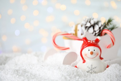 Photo of Christmas composition with decorative snowman on artificial snow against blurred festive lights, space for text