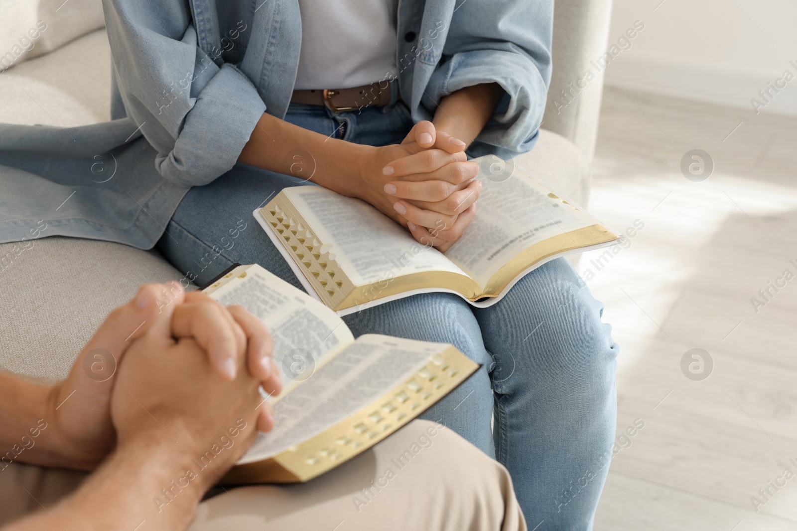 Photo of Religious people with Bibles praying together indoors, closeup