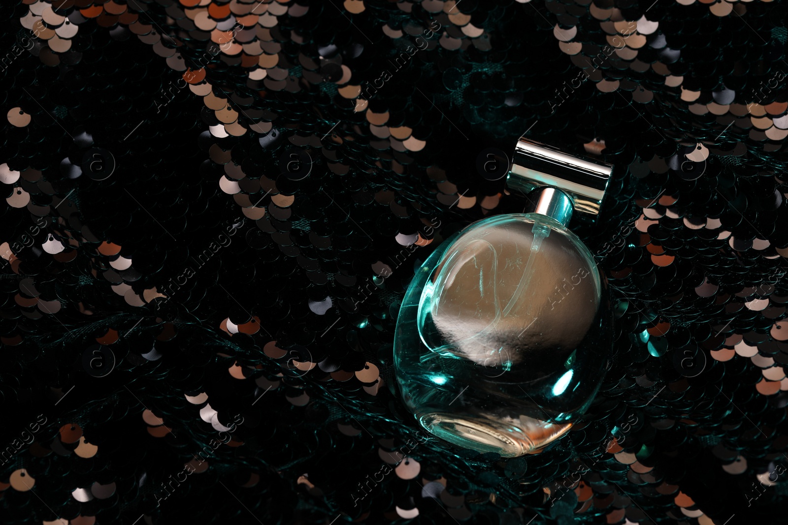 Photo of Luxury perfume in bottle on fabric with shiny sequins, above view