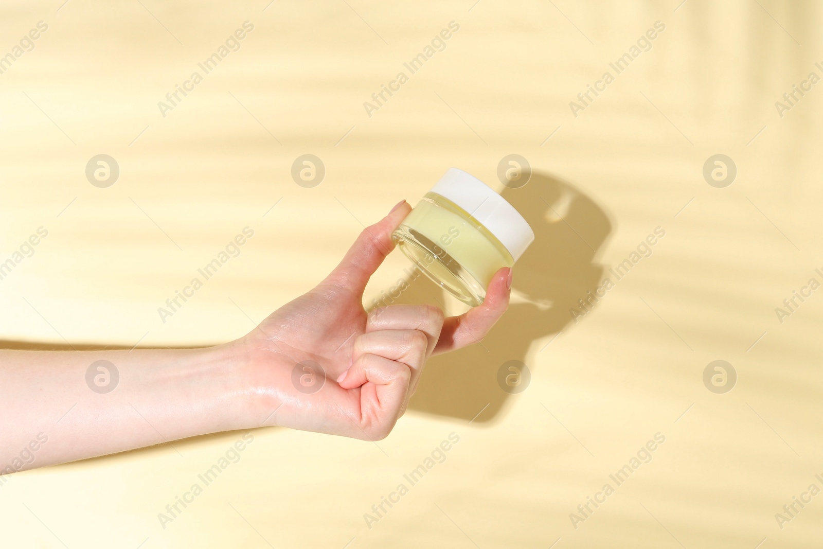 Photo of Woman holding jar of cream on yellow background, closeup