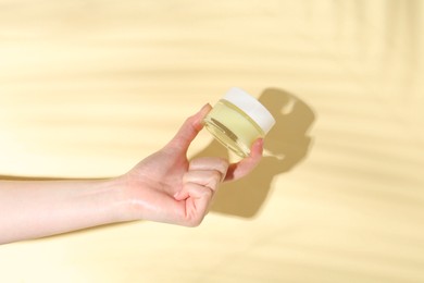 Photo of Woman holding jar of cream on yellow background, closeup