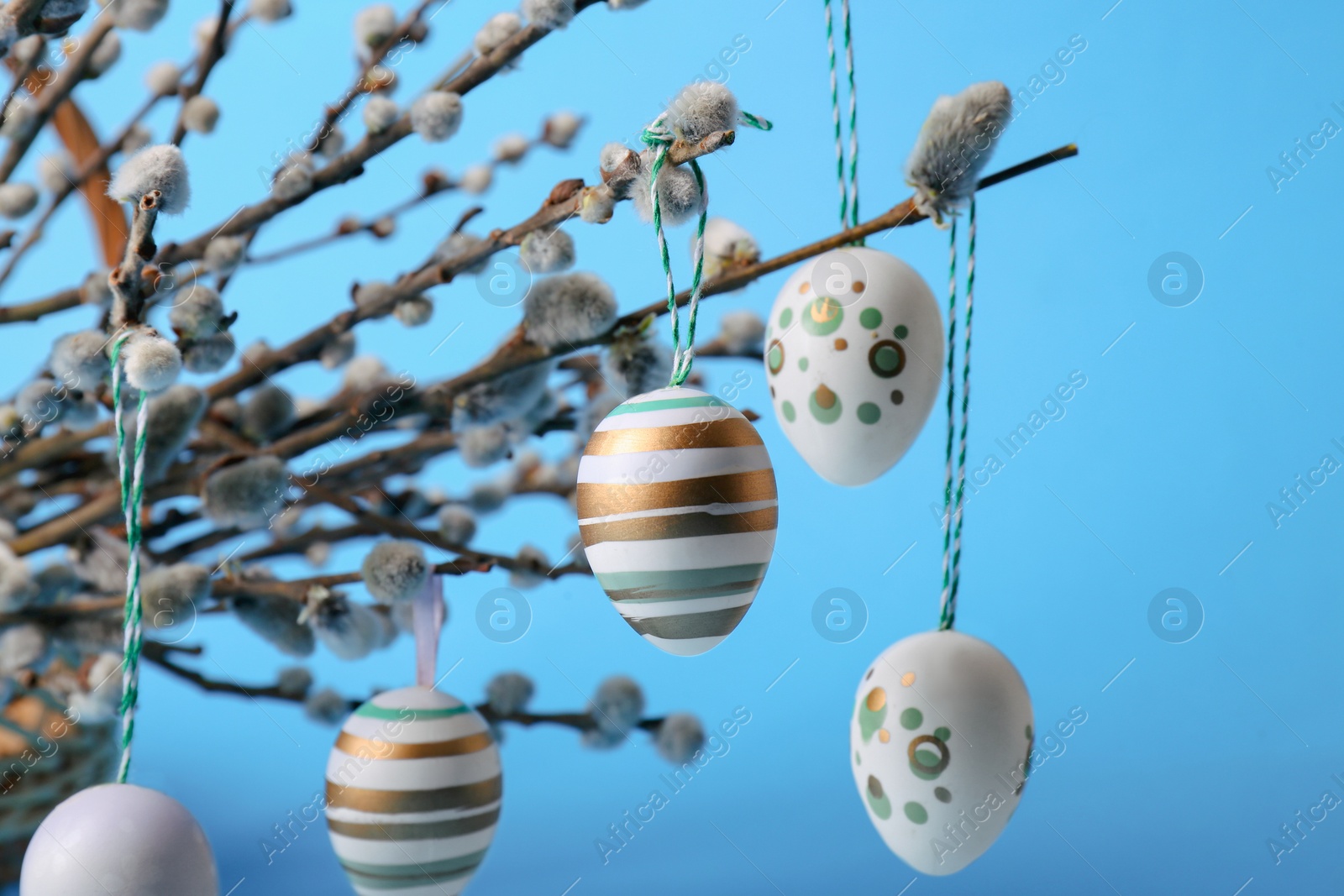 Photo of Beautiful willow branches and painted eggs on light blue background, closeup. Easter decor
