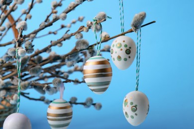 Beautiful willow branches and painted eggs on light blue background, closeup. Easter decor