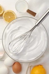 Photo of Bowl with whipped cream, whisk and ingredients on white wooden table, flat lay
