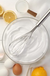 Bowl with whipped cream, whisk and ingredients on white wooden table, flat lay