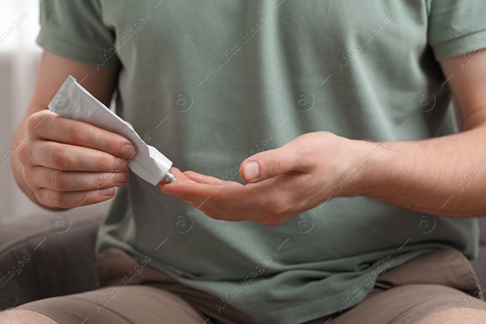 Photo of Man applying ointment from tube onto his fingers indoors, closeup