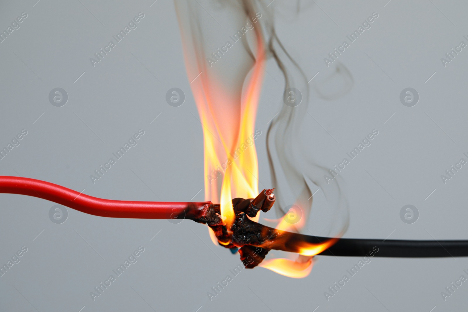 Photo of Inflamed red wire on grey background, closeup. Electrical short circuit