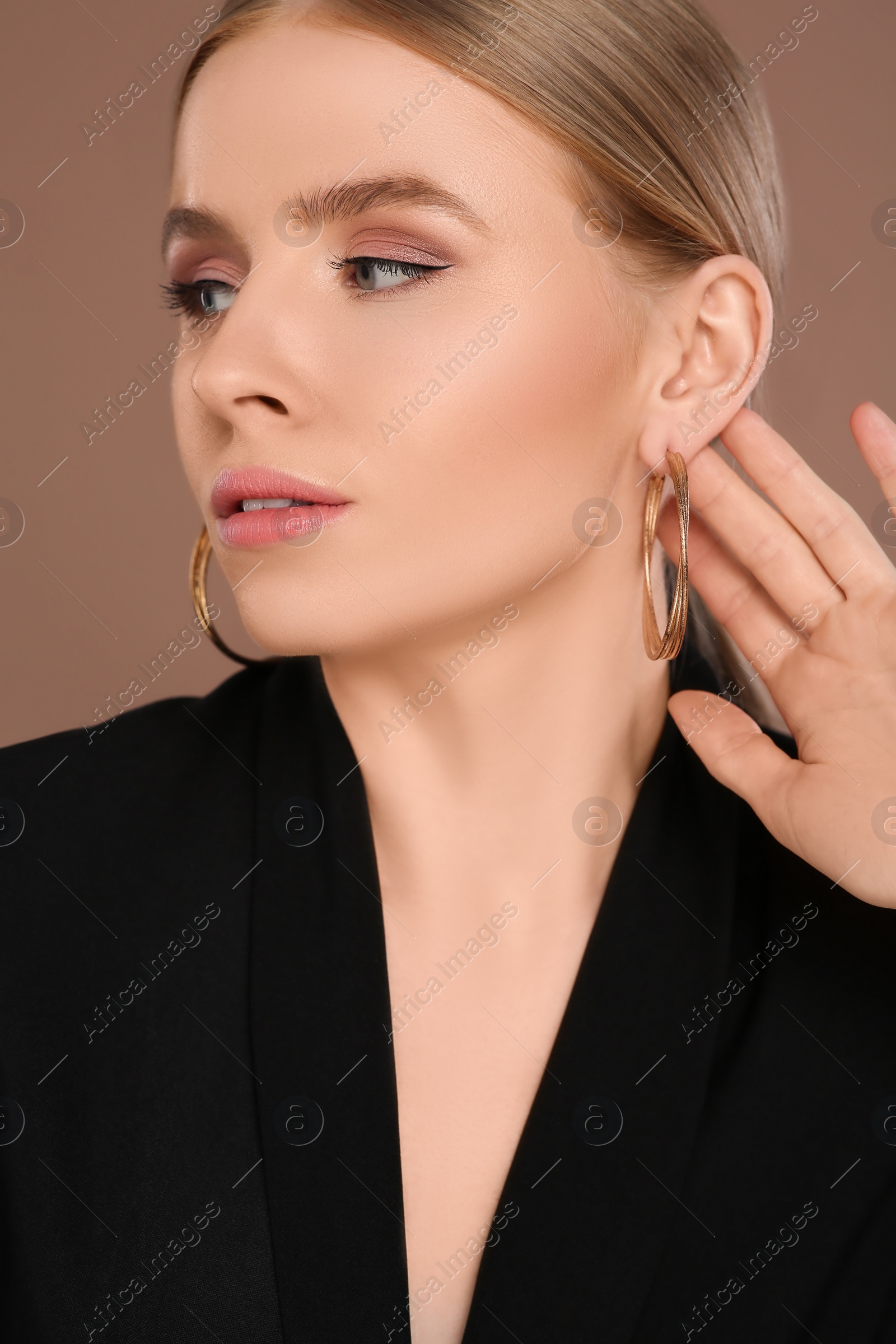 Photo of Beautiful young woman with elegant earrings on light brown background