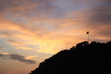 Photo of Picturesque view of trees and flag on hill at sunset, space for text