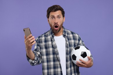 Photo of Emotional sports fan with soccer ball and smartphone on purple background