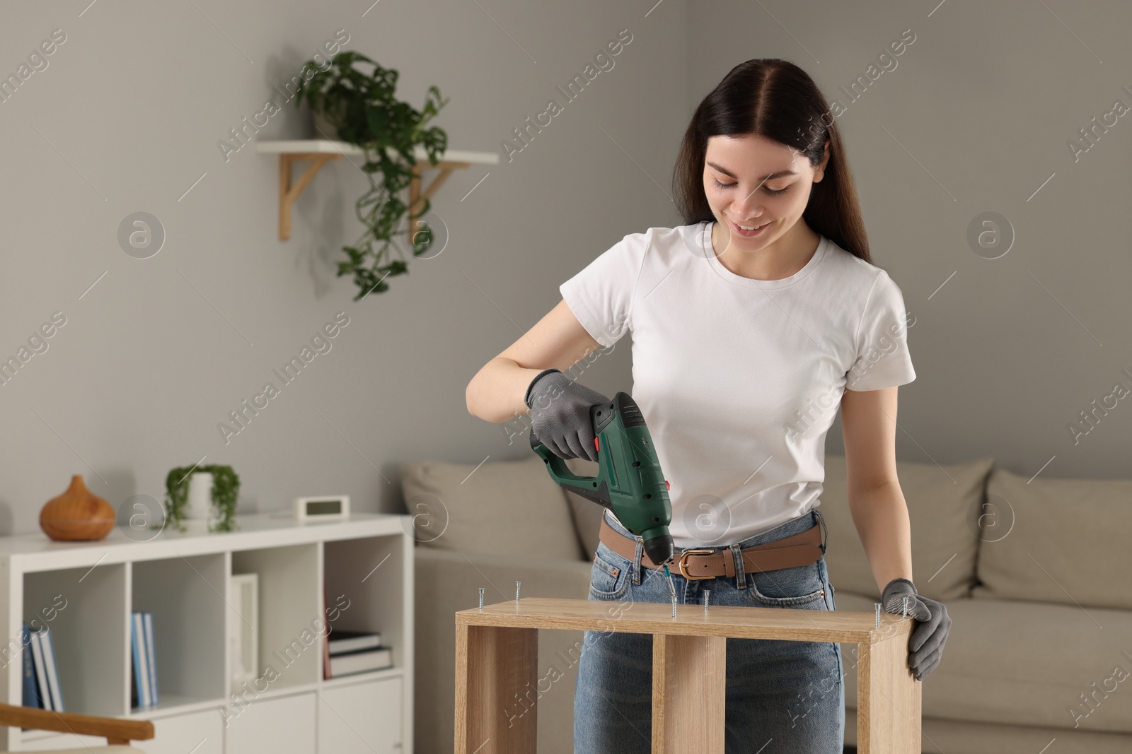 Photo of Young woman with electric screwdriver assembling furniture at home. Space for text