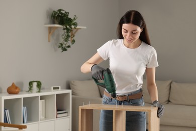 Young woman with electric screwdriver assembling furniture at home. Space for text